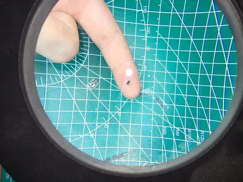 ATtiny10 microcontroller chip viewed through a loupe next to a small breakout board