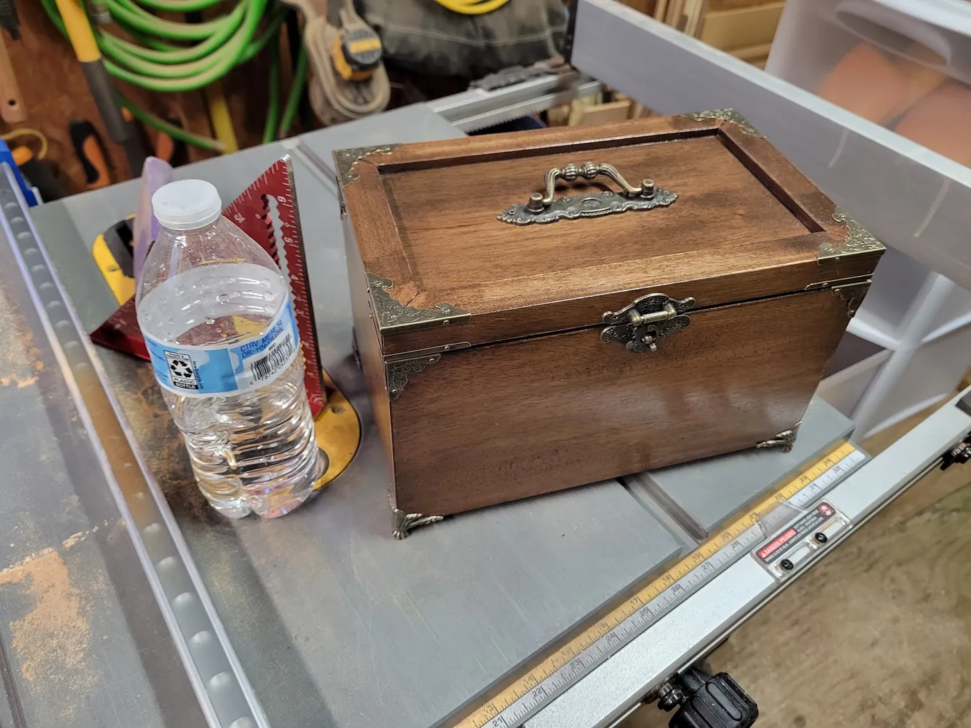 Finished mahogany jewelry box with antique brass hardware, closed, next to a water bottle for scale