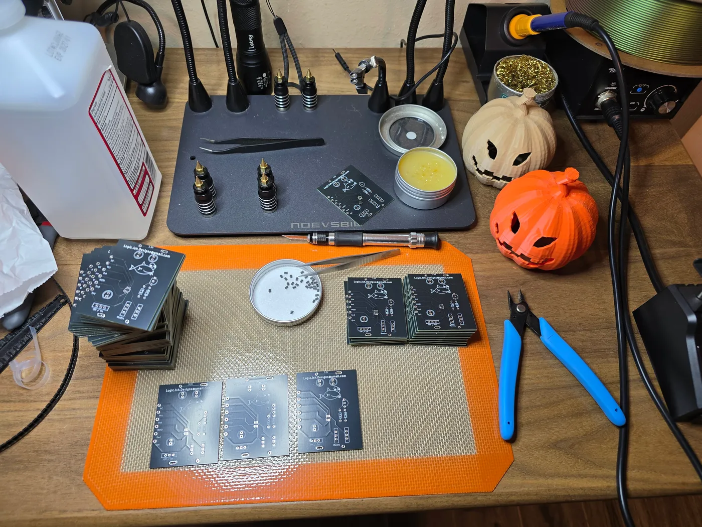 Workbench with dozens of finished custom PCBs and two 3D-printed jack-o'-lantern shells