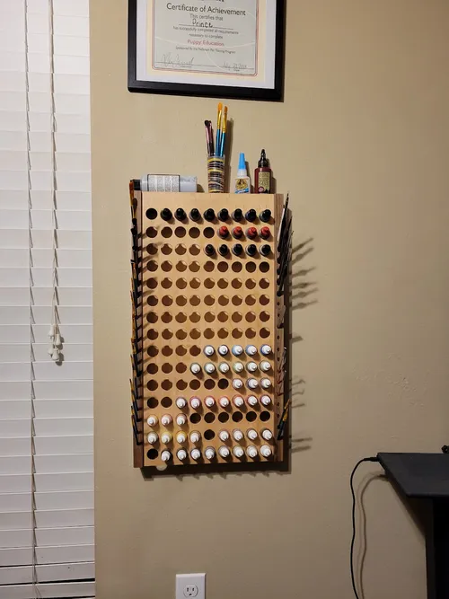 Finished wall-mounted paint rack loaded with paint bottles and brushes