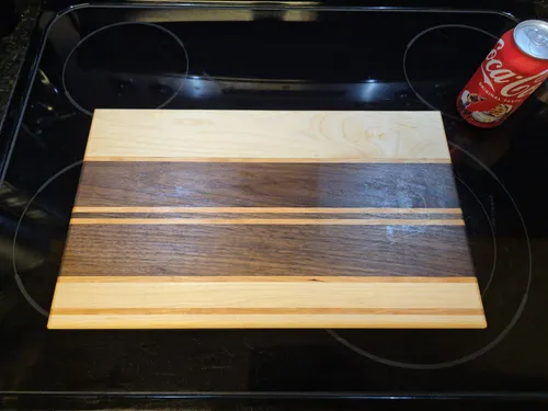Finished walnut and maple striped cutting board next to a soda can for scale
